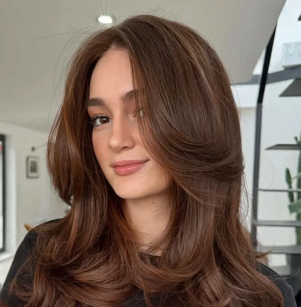 Close-up of a young woman with long auburn hair and soft makeup, indoors, looking at the camera.
