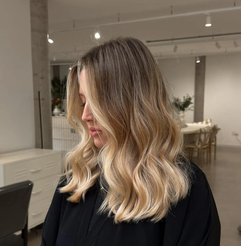 Side profile of a woman with long, wavy blonde hair in a modern hair salon.