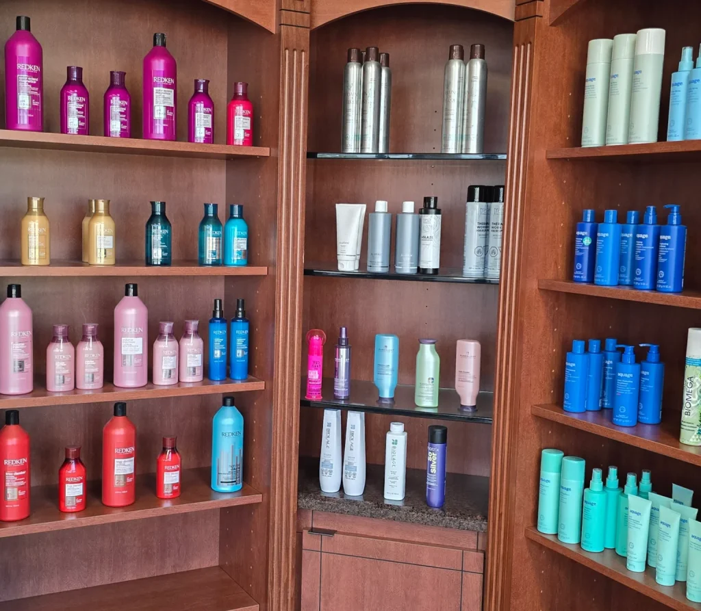 Shelf filled with colorful hair products (pink, purple, gold, blue, and teal bottles) in a wooden display cabinet at a salon.