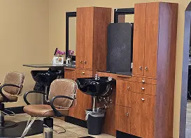 Hair salon interior with wooden styling stations, round mirrors, and brown chairs beside wash basins.