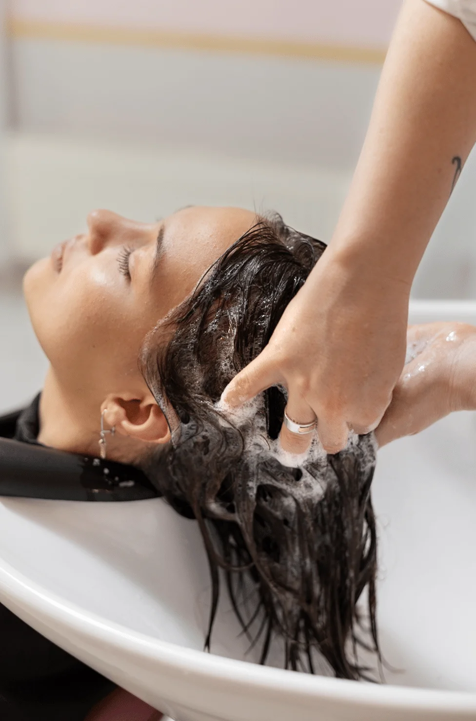 Person lying back in a salon sink as a stylist washes their hair, lather and foam visible around the scalp and temples